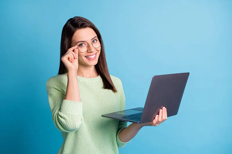 Autoba - Eine Frau mit Brille hält einen Laptop in der linken Hand und mit der rechten Hand hält sie vorsichtig an ihrer Brille.